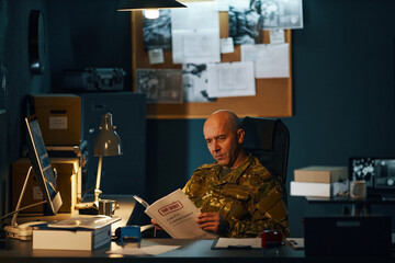 Man in military uniform working at the office late night, reviewing important documents and...
