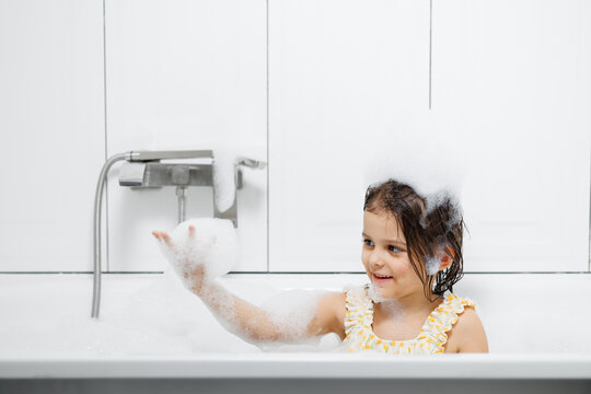 little girl bathes and washes her hair in soap suds.