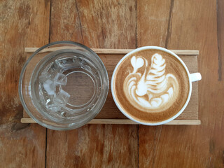 A cup of latte art coffee with drinking water on wooden background.