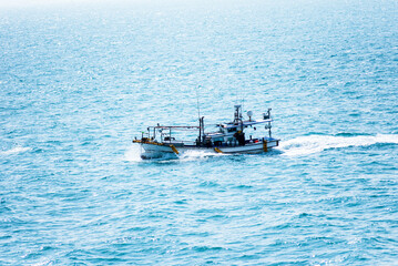 Small fishing boat sailing through blue, calm ocean.