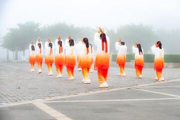 In the foggy morning at the park square, people engage in Tai Chi fitness exercises