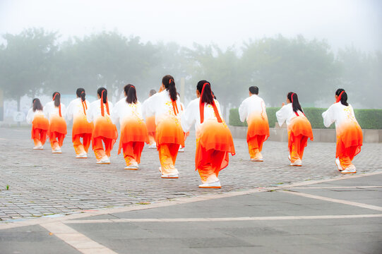 In the foggy morning at the park square, people engage in Tai Chi fitness exercises - Powered by Adobe