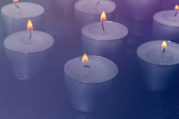 Tea light candles on a dark background, many lights in the dark, candlelight, toned image