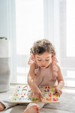 Vertical photograph of a little girl playing in her room with a wooden letter puzzle. Fun and learning in childhood. Development of cognitive and motor skills. Montessori education.