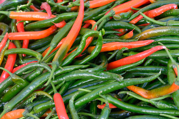 Vibrant green and red chili peppers piled together at a bustling local market during daytime