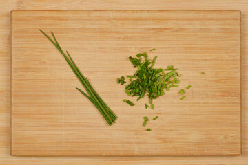 A top-down shot of a wooden cutting board with a small bunch of whole chives and a pile of chopped chives