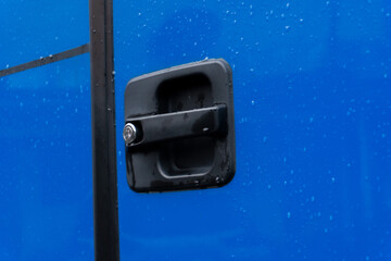 A close-up of a black door handle with a keyhole on a blue surface covered in raindrops.