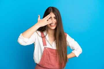 Young caucasian woman isolated on blue background covering eyes by hands and smiling