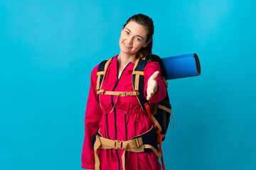Young mountaineer woman over isolated blue background shaking hands for closing a good deal