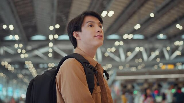 Asian male tourist looking around to find his way to the boarding gate inside the airport terminal. Male tourist passenger excited to go travel abroad by airplane for holiday vacation trip.