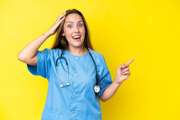 Young surgeon nurse woman isolated on yellow background surprised and pointing finger to the side