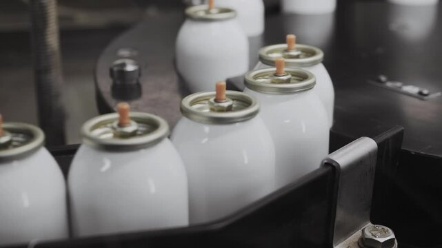 Empty aerosol cans moving on conveyor belt in spray can factory.