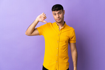 Young Colombian man isolated on purple background showing thumb down with negative expression