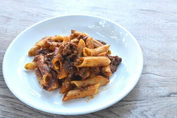 baking penne pasta topping mashed beef meat in sweet and sour sauce on plate    