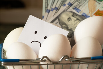 Chicken eggs in a supermarket basket on the table and a sad drawing on paper and dollars in the...