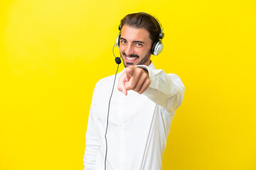 Telemarketer caucasian man working with a headset isolated on yellow background points finger at...