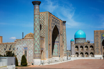 Registan Square in Samarkand, Uzbekistan, a historic architectural ensemble featuring three stunning madrasas with intricate mosaic designs, domes, and minarets under a bright blue sky