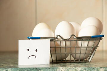 Chicken eggs in a supermarket basket on a table and a sad drawing on paper in the kitchen, egg...