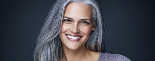 Smiling woman with long gray hair against dark background showcasing confidence and beauty