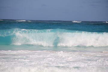 Turquoise ocean waves surging against white sandy shoreline, breaking with thunderous force under blazing sunlight, revealing dynamic marine landscape