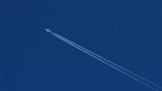 The journey begins, plane flies high in the blue sky, leaving a white trail. Jet airplane flying overhead in clear blue sky and leaving nice contrail. Plane smoothly as it flies through the sky