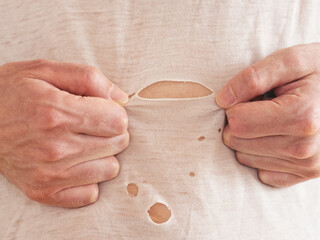 A man inspecting a ripped t-shirt that he is wearing. Close up.