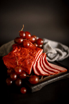meat balyk on a wooden board with purple large grapes on a black background
