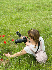 Woman lying in a green meadow photographing red poppies with a professional camera.