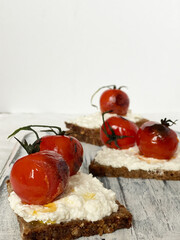 Close-up of whole grain bread slices topped with creamy ricotta cheese and roasted cherry tomatoes.