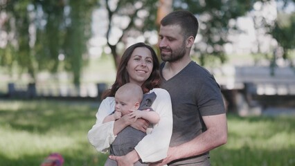 On a sunny day, a joyful family enjoys quality time together at the park, smiling with their cute baby