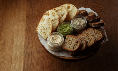 Assorted artisan bread slices with three types of butter in glass jars on a rustic wooden table. A delicious selection of fresh bakery and butter for breakfast or snack.
