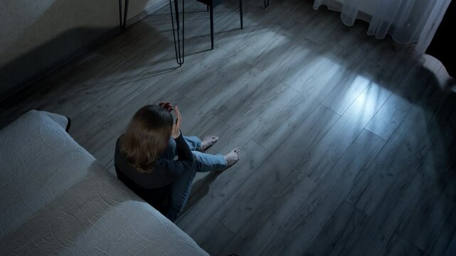 Lonely woman sitting on the floor in a dark room. Concept of problems, depression and stress. Mental health. Domestic violence.