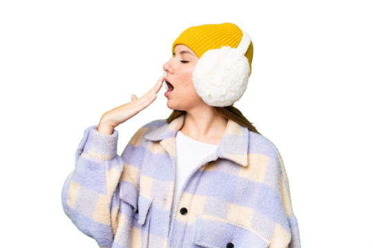Young blonde woman wearing winter muffs over isolated chroma key background yawning and covering wide open mouth with hand - Powered by Adobe