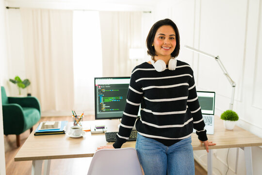 Hispanic software developer smiling while coding on laptop at modern home workspace