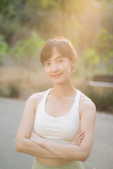 Asian woman outdoor workout. Healthy and active lifestyle concept. She smiles confidently in serene park setting with sunlight filtering through