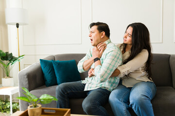Woman performing heimlich maneuver on choking partner during urgent health crisis in home living...