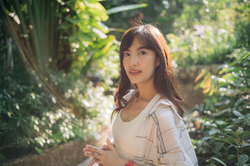 Asian woman enjoying summer while breathing fresh air in lush green garden, surrounded by vibrant...
