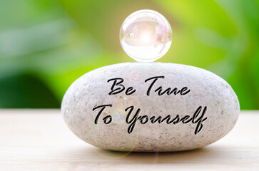 Close up of Zen stone with Be True To Yourself text on the stone. Self reflection concept