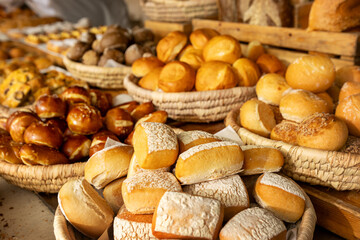 Close-up of freshly baked bread rolls and pretzels in rustic wicker baskets at bakery market. Variety of golden, crusty and whole grain bread selection
