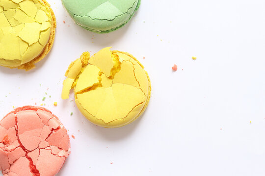 Bright multi-colored French macarons on a light background, top view. Assortment of macarons with different flavors. Delicious pastries. Crumpled macarons, flat lay. Broken macaron on white background