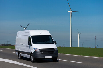 White electric delivery van on the road. Wind turbines in the background.