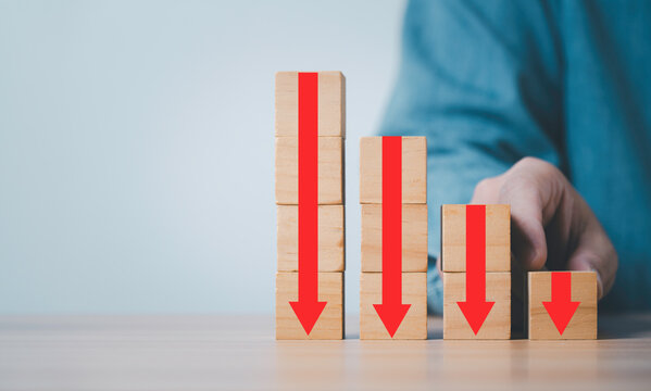 Businessman holding red down arrow which print screen on wooden block cube and copy space for cost profit economy and benefit decreasing concept.
