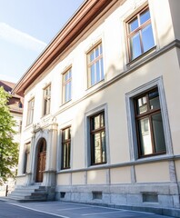 Fototapeta premium This historic building features intricate architectural details with large windows reflecting the clear sky. The surrounding area is calm, showcasing a well-maintained environment