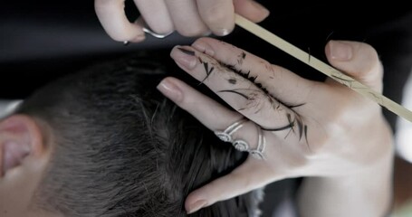 Barber doing a haircut to male client in barbershop close up. Close up of a Barber scissor cutting a young mans hair.