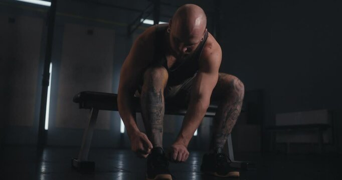 Portrait of a jock man with earrings in his ears tying his sneakers before starting a strength training session in the gym