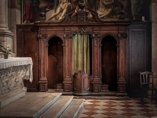 A vintage wooden confessional with intricate carvings and a green curtain, symbolizing faith, repentance, and tradition in a sacred religious setting.
