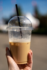 Plastic transparent cup and straw, iced latte on sunny day in a woman hand