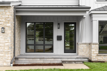 A modern farmhouse front door detail with large black framed windows and front door, grey board and...