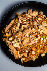Wok noodles with chicken meat and sesame and peanut in bowl on dark stone background 