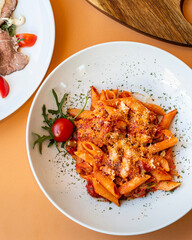 Delicious penne pasta arabiata with tomato sauce, and cheese on served white plate, flat lay
